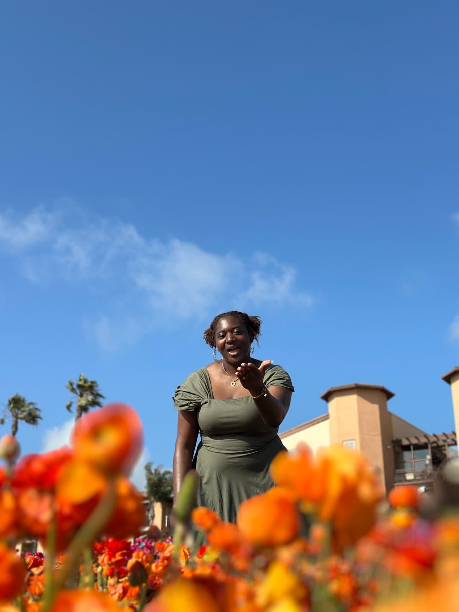 A woman in a green dress reaching toward the camera, shot low through orange flowers under a blue sky